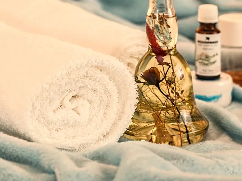 Linge de massage roulé et flacon d'huile posés sur une couverture